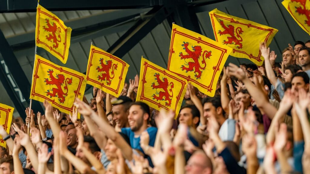 Fans waving the lion rampant flag at a rugby match.